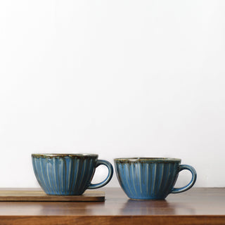 Set of blue glaze ceramic broad cups with handles and line ribbed detailing, on wooden table, one elevated on wooden slab. Buy kitchenware Bangalore.