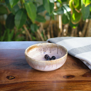 A compact size sleek light pink glazed ceramic bowl with brown drip glaze detailing, filled with grapes on a table outdoors. Explore handcrafted ceramics in India.