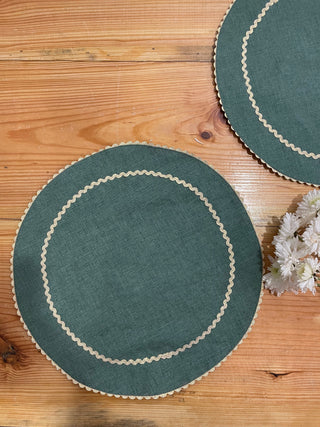 Two round dark green round table mats with gold zari scallop border and inner circle, with white flower on a wooden table. Explore unique gifting ideas in Bangalore