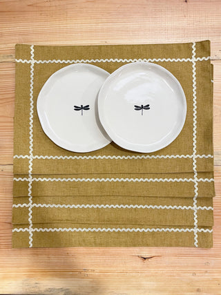 4 mustard rectangle table mats with gold scallop lace creating check at corners, top mat with 2 ceramic plates. Buy tableware online in India.