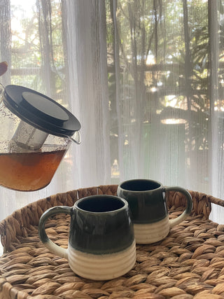 Short belly ceramic mug green glaze top half, stoneware ribbed texture bottom half. On crane tray, green tea being poured. Shop ceramics for Indian homes.