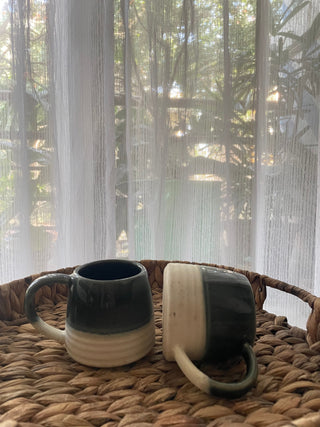 Pair of small ceramic mugs with big handles: green glaze top half, white stoneware ribbed finish bottom half. One upright, one flat on crane tray. Shop designer tableware India