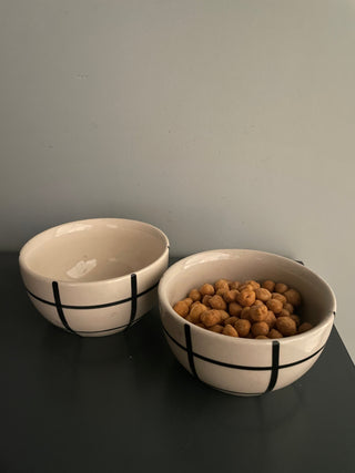 Pair of small ceramic katori bowls, elegantly hand-painted with broad black checks; one bowl with snacks. Explore home decor gifts in India.