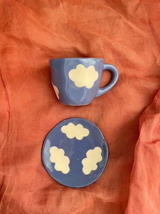 Top shot of blue glaze cup & saucer with stoneware finish cloud motifs, placed flat on orange cloth. Explore unique gifting ideas India.