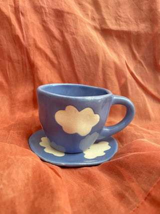 Blue cup & saucer set in blue glaze with off-white cloud motifs in stoneware finish on orange cloth. Buy artistic ceramics India.