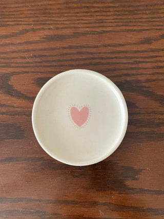 A small round off-white coaster with pink heart design kept on wooden table. Shop artistic ceramics Bangalore.