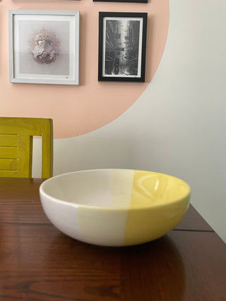 Medium white, light yellow, yellow glaze ceramic bowl in symmetrical design on wooden dining table with yellow chair and wall art. Shop designer tableware India