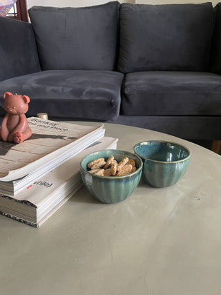  Living room: cement table, 2 books with bear-shaped candle, and 2 green ceramic bowls (one filled with Indian sweets). Shop ceramics Bangalore.