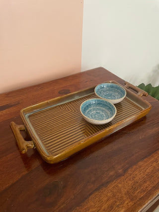 Medium rectangular ceramic platter in beige with ribbed design, handles, on wooden table. Two small blue pattern dip bowls inside. Explore unique gifting ideas Bangalore.