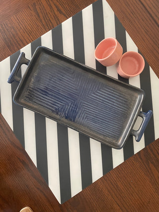 Medium rectangular ceramic platter with handles, blue shiny glaze ribbed design, on B&W stripe mat with 2 small pink dip bowls. Shop handcrafted ceramics India.