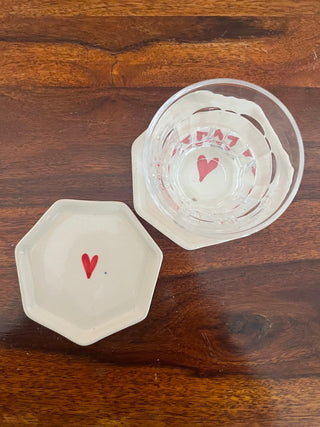 Set of 2 hexagon off-white coasters with hand-painted heart in the middle, one with a glass of water on wooden table. Shop ceramics for Indian homes.