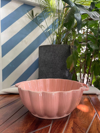 A classy pink glazed bowl with scallop rim, short handles, and tonal line detailing, placed outdoors on a table. Dive into ceramics for Indian homes.